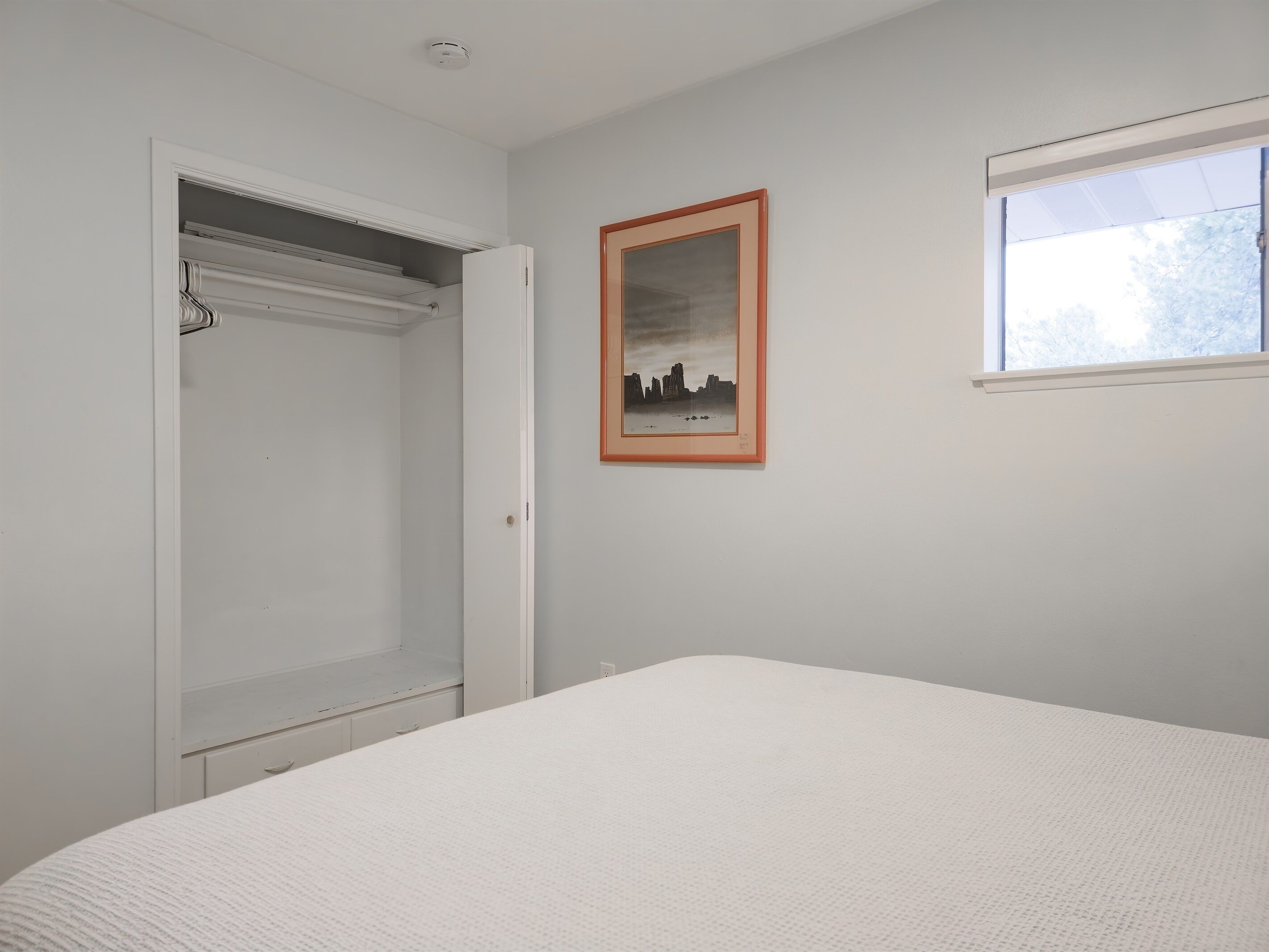 Ein Schlafzimmer mit Bett, Kleiderschrank, einem gerahmten Bild an der Wand und einem Fenster.