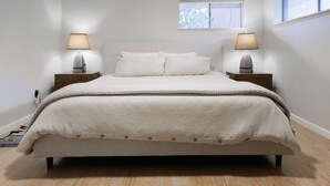 A bedroom with a large bed, two bedside tables with lamps, a window, and a small skylight. - Sedona Retreat with Red Rock Views, Mid-Century Charm | Upper Level Duplex (Sedona)