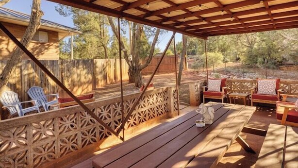 An outdoor patio with wooden furniture, including chairs and a table, and a decorative fence. - Sedona Retreat with Red Rock Views, Mid-Century Charm | Upper Level Duplex (Sedona)