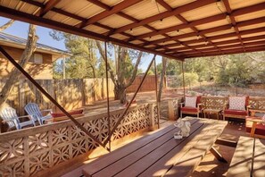 Eine Terrasse im Freien mit Holzmöbeln, darunter Stühle und ein Tisch, und einem dekorativen Zaun.
