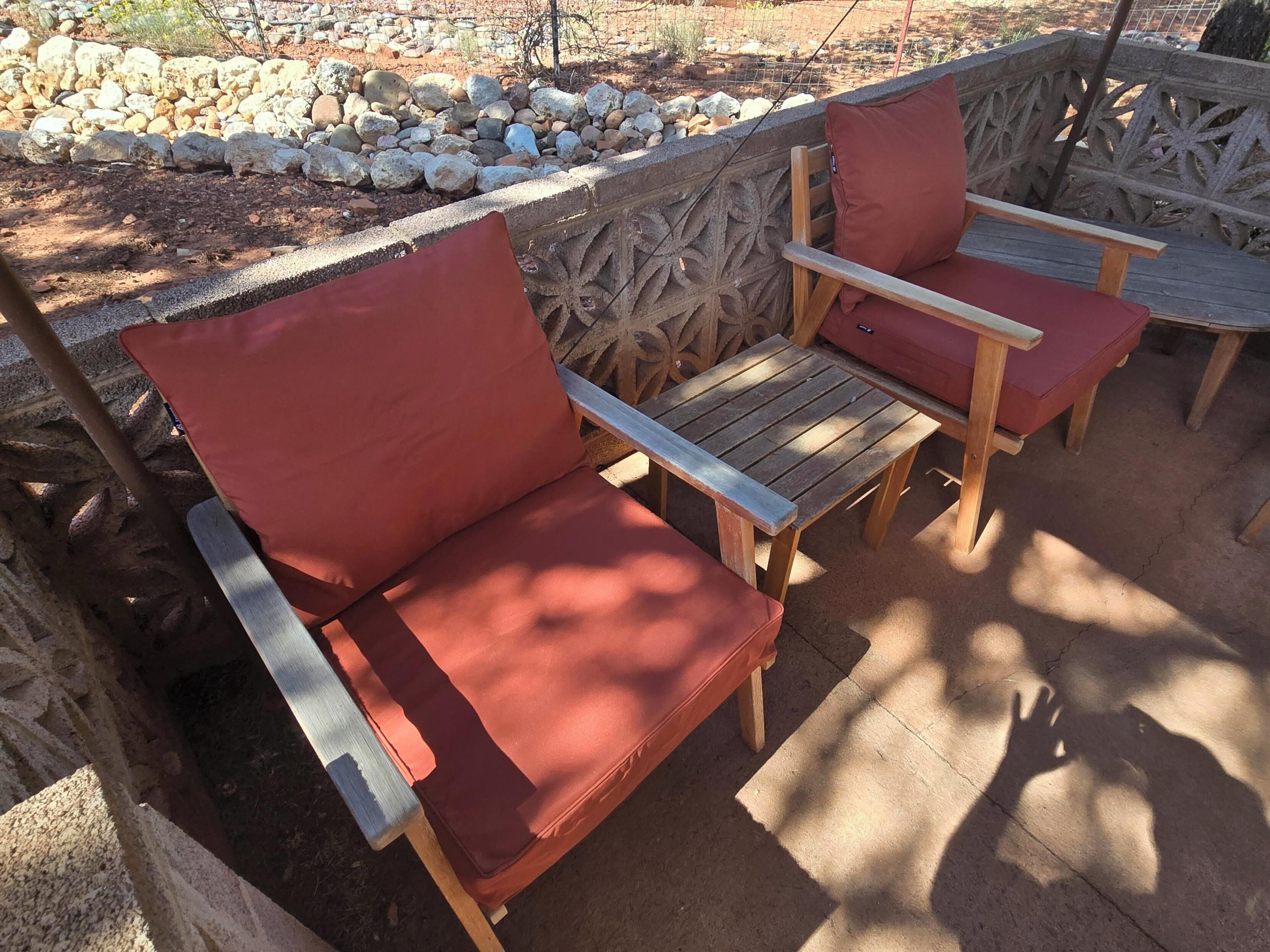 A patio area with two wooden chairs and a table, surrounded by a decorative stone wall.