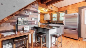 A kitchen with wooden walls, a stainless steel refrigerator, and a bar area with stools.