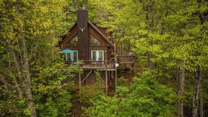 A cabin with a deck and a covered outdoor seating area, surrounded by dense forest.