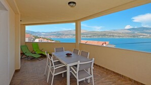 Uma varanda com mesa e cadeiras, vista para uma cidade costeira e uma cordilheira ao longe.