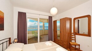 Quarto com cama, guarda-roupa de madeira, cadeira, espelho e vista para o mar através de uma porta de correr.