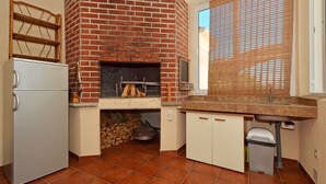 Uma cozinha compacta com forno de tijolos, geladeira e janela com persianas.