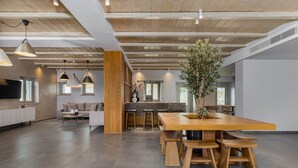 A spacious living area with a large wooden dining table, multiple seating options, and a kitchen area in the background. - Salvia Areopolis All-Suite Hotel (East Mani)