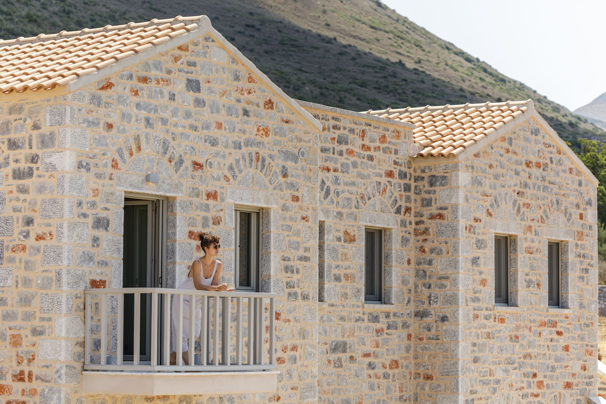 A stone building with a tiled roof, a balcony with a railing, and windows.