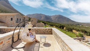 A stone building with a balcony, a hanging chair, and a small table. - Salvia Areopolis All-Suite Hotel (East Mani)