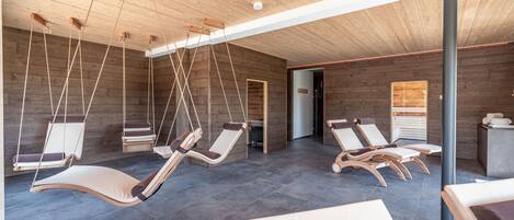 Un espacio de spa con paredes de madera, sillones de masaje colgantes y un diseño moderno en el techo.