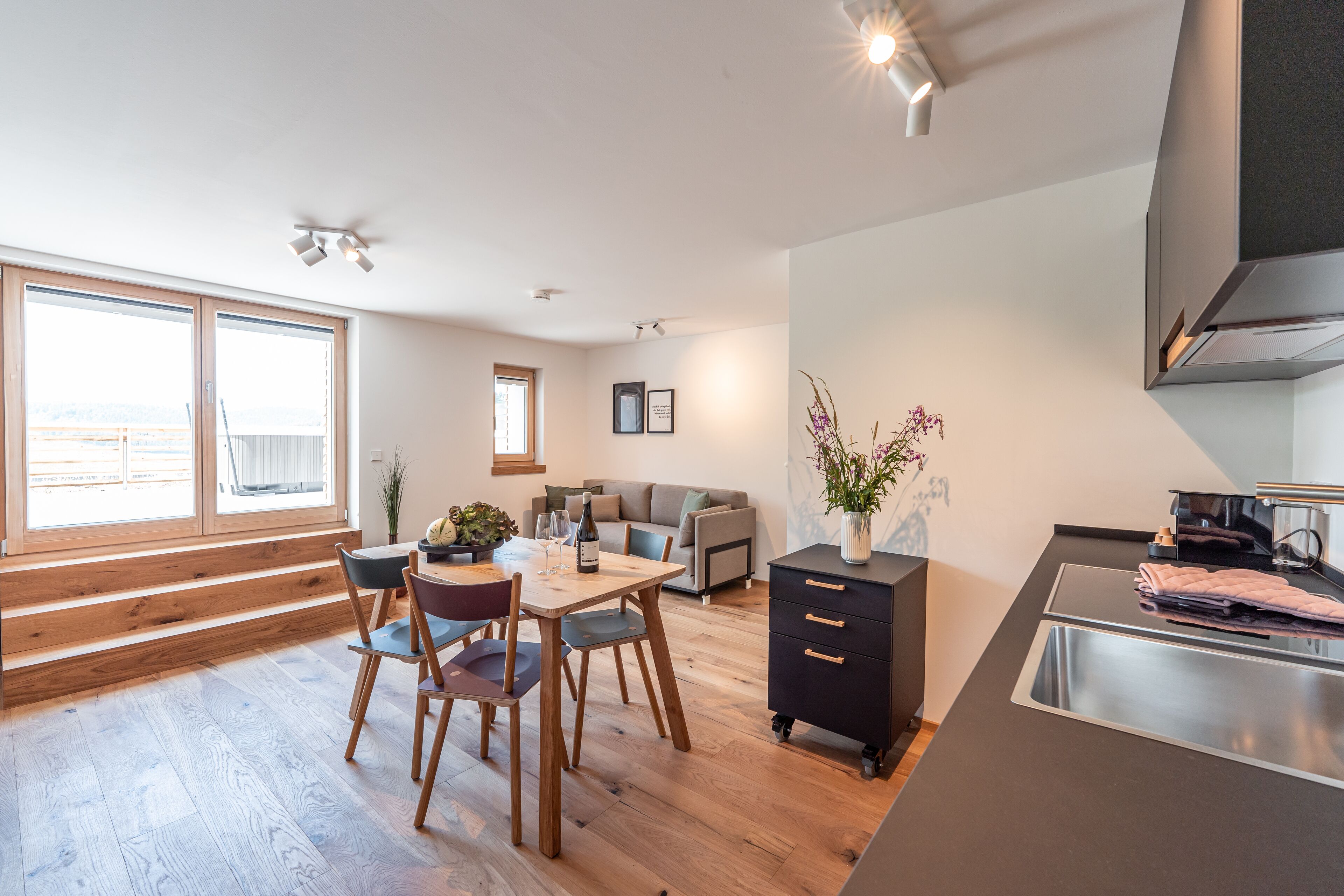 Une cuisine moderne dotée d’une cuisinière intégrée, un coin repas avec une table et des chaises en bois, et une grande fenêtre offrant une vue dégagée.