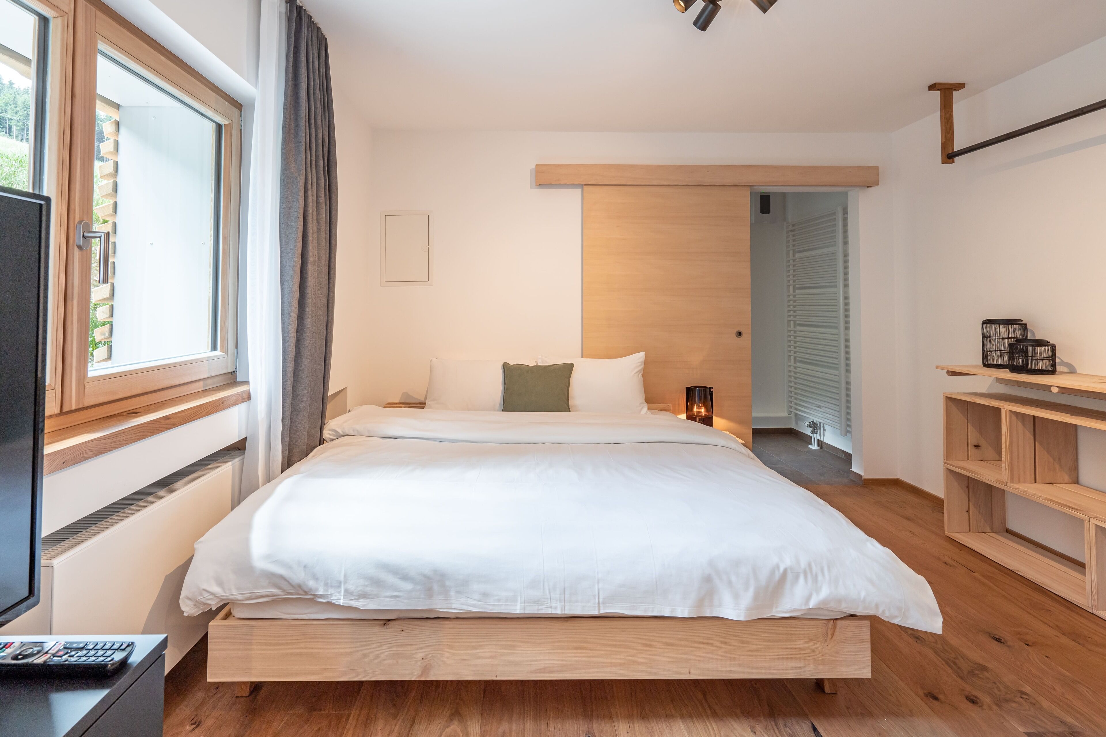 Une chambre moderne avec un lit en bois, une table de chevet avec une lampe et une vue sur un couloir.