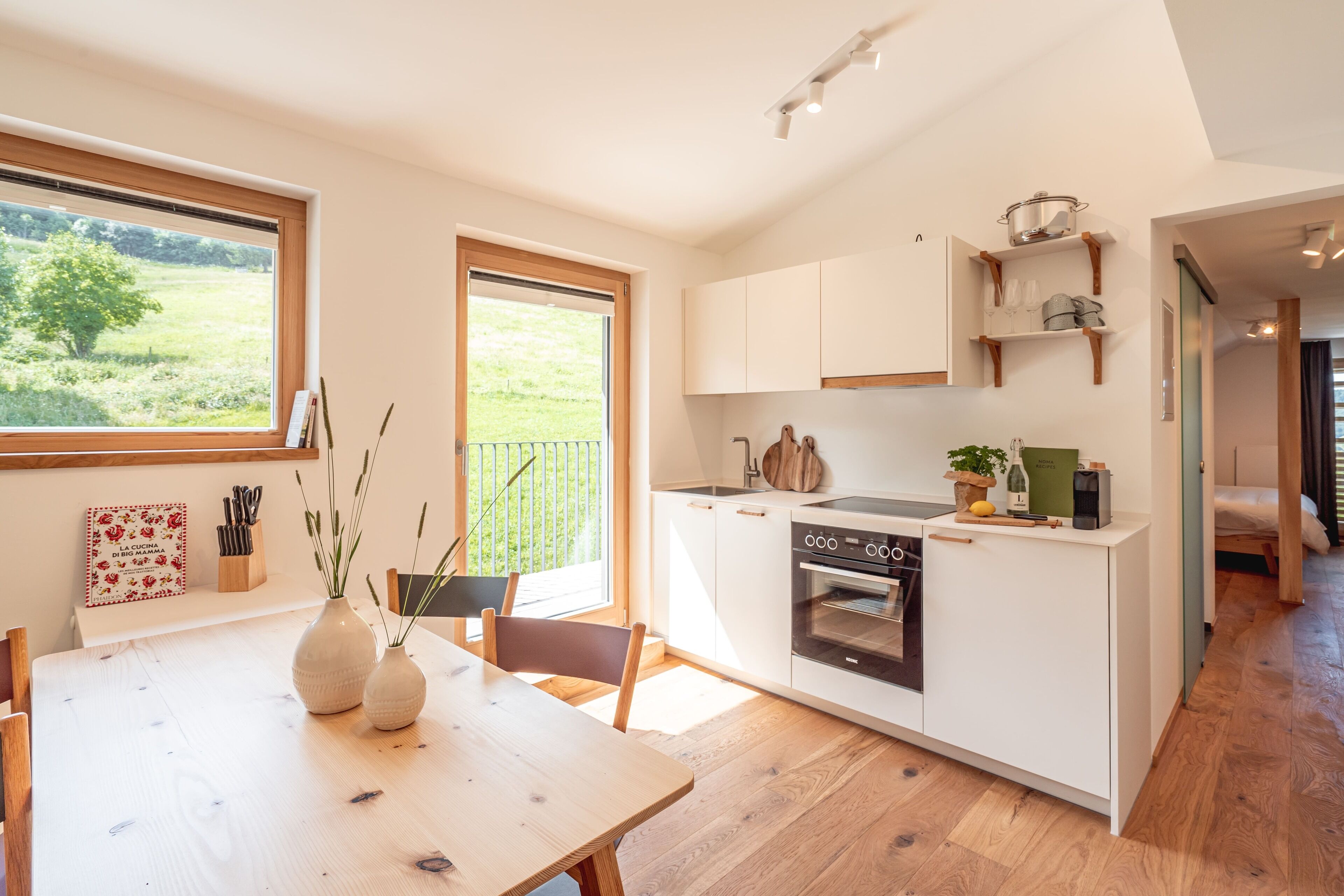 A modern kitchen with white cabinetry, a built-in oven, and a window overlooking a green landscape.