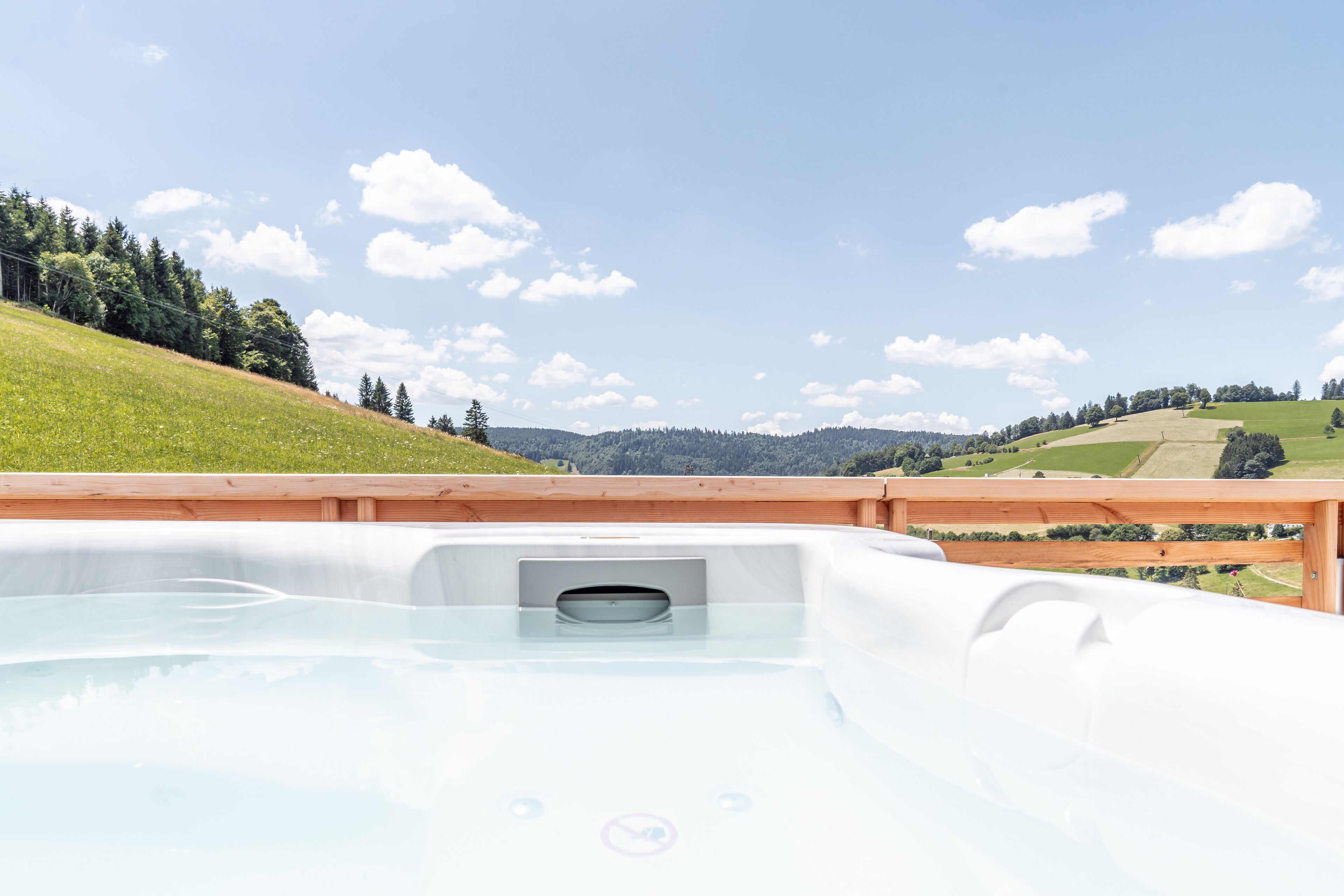 A hot tub with a wooden deck and a scenic view of rolling hills and trees.