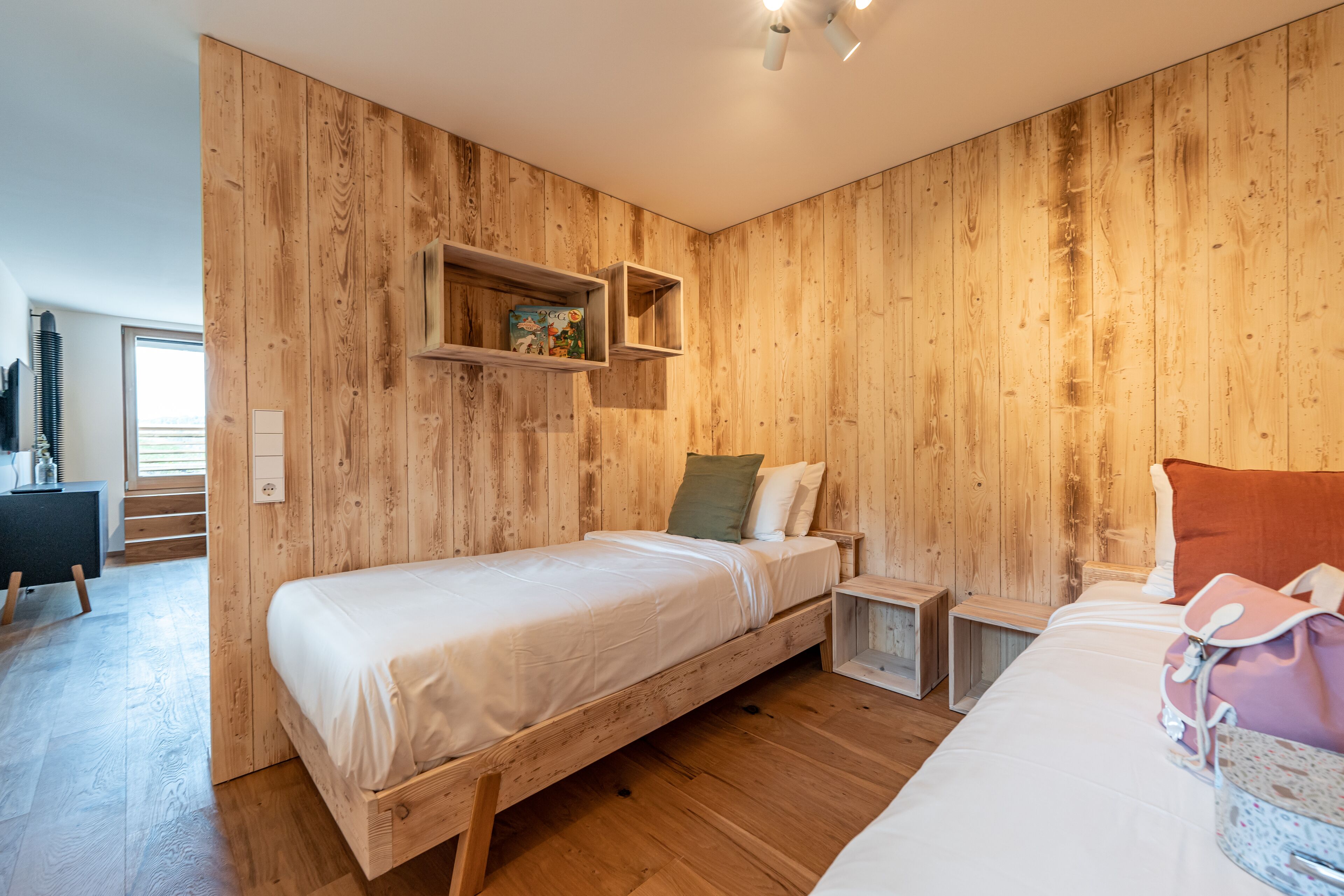 Una habitación con paneles de madera, una cama, mesitas de noche y un estante con un juguete.