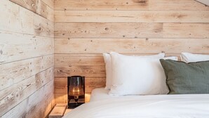 A bedroom with wooden panel walls, a bed with white and green pillows, and a nightstand with a lamp. - stuub todtnauberg (Todtnau)