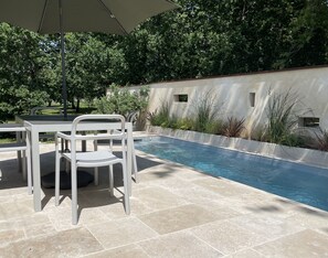 A swimming pool with a tiled deck, surrounded by a low wall and plants.