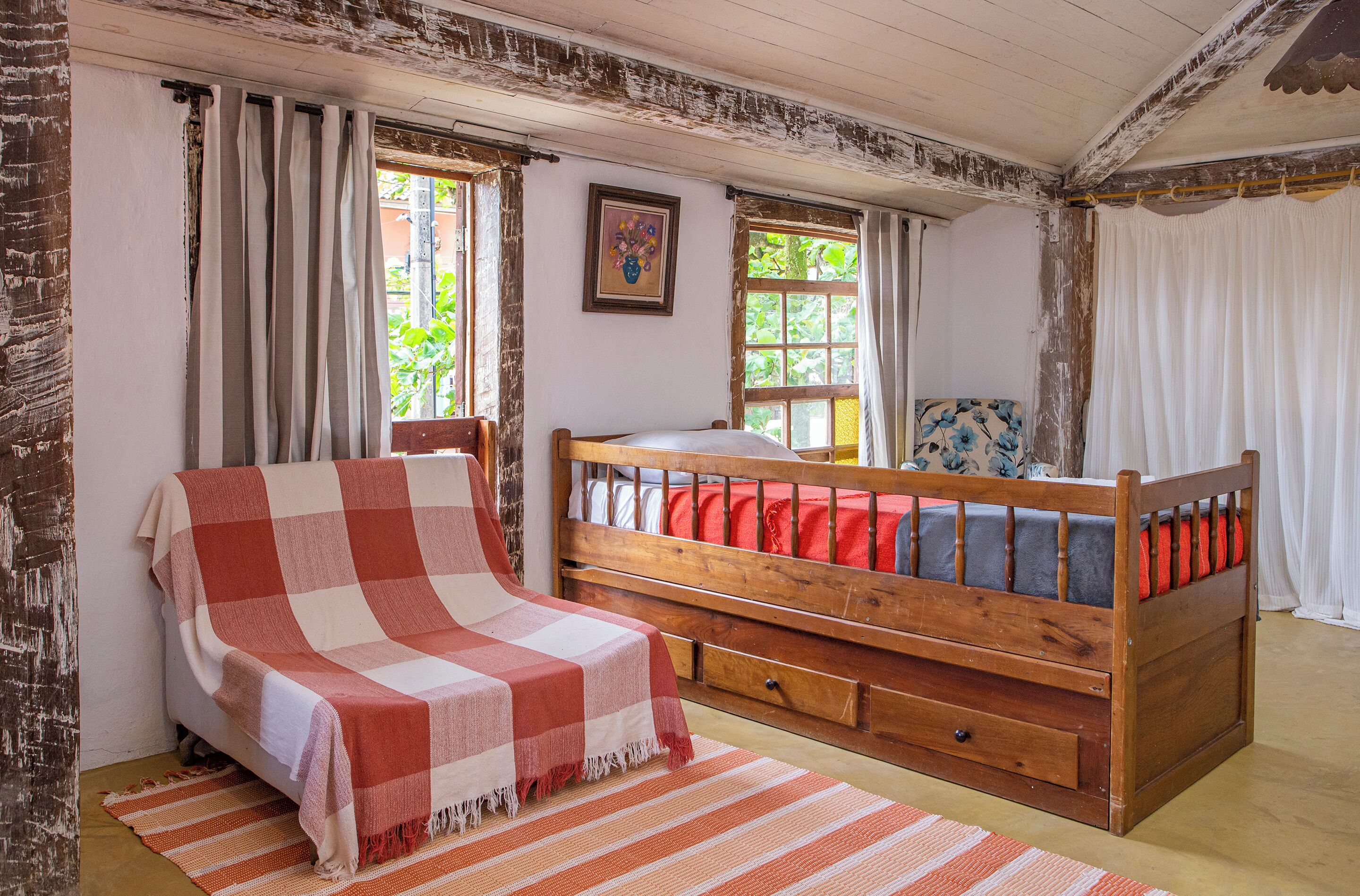 A rustic bedroom with a wooden bed, a small bedside table, and a window with curtains.