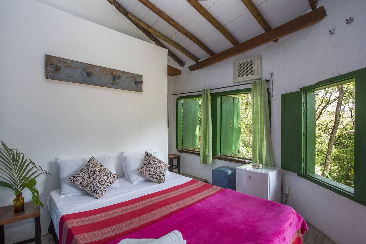 Une chambre à coucher avec un lit, une fenêtre avec des volets verts, un radiateur et un plafond en bois.