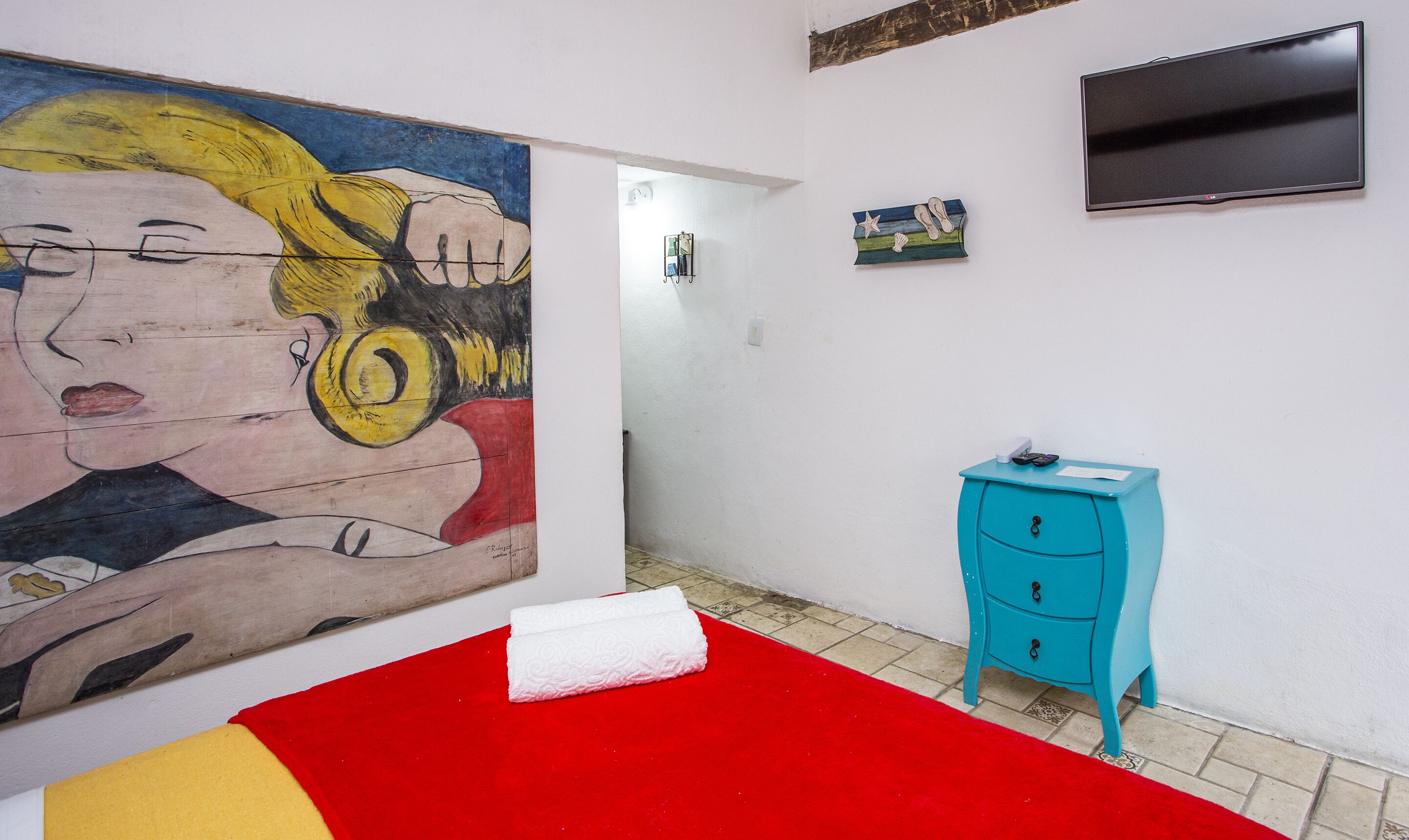 Um quarto com uma cama, um quadro, uma televisão e um pequeno armário azul.