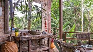 Een houten tafel in rustieke stijl met een plant in pot, een schaal en een theepot op een terras met rieten stoelen.