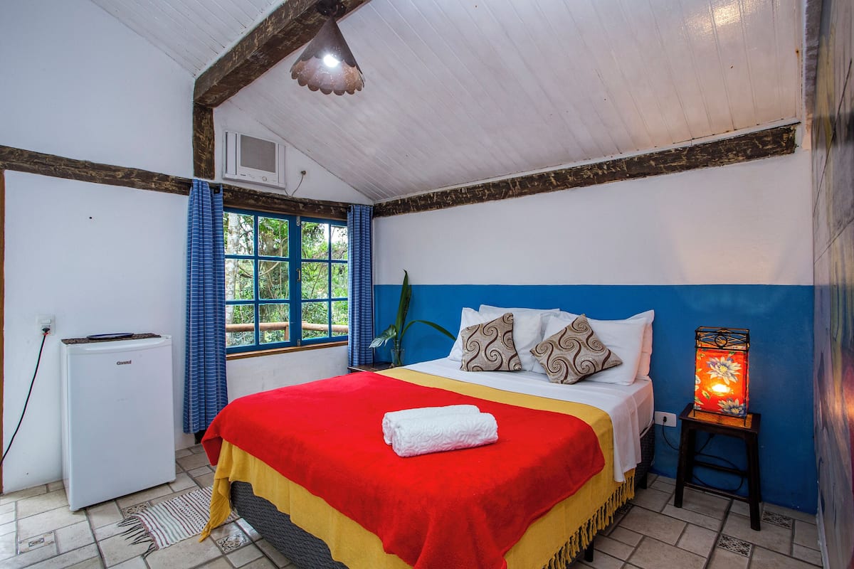 Une chambre à coucher comprenant un lit, un radiateur, une fenêtre avec des rideaux et une table de chevet avec une lampe.