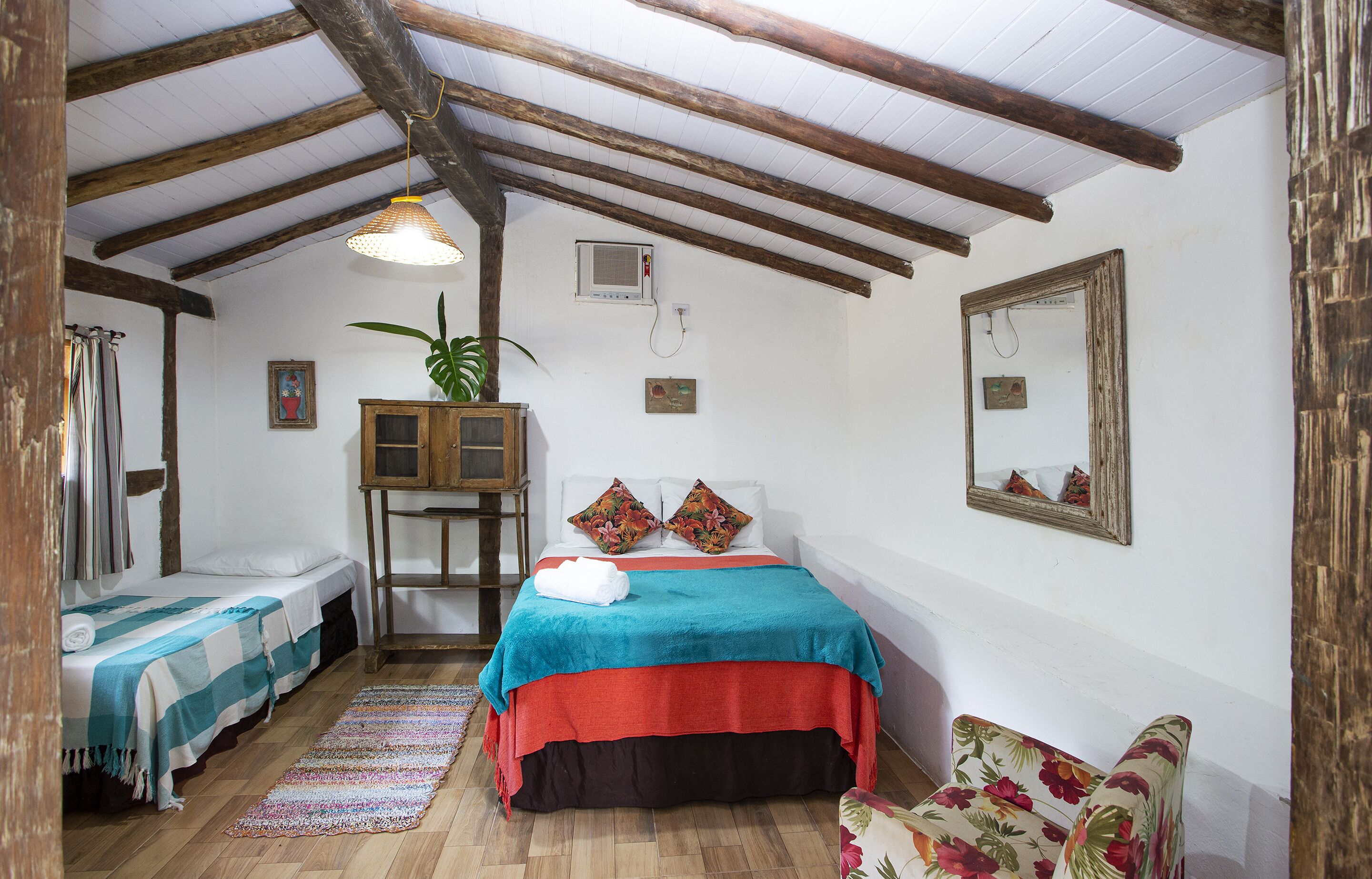 A room with a bed, two bedside tables, a mirror, a potted plant, and a floral chair.