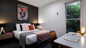 Moderni hotellihuone, jossa on suuri sänky, yöpöydät, työpöytä ja ikkuna, josta avautuu näkymä vehreään maisemaan.