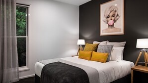 Quarto moderno com uma cama grande, duas luminárias de cabeceira e uma obra de arte emoldurada na parede.