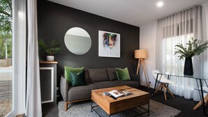 Uma sala de estar moderna com um sofá cinzento, um espelho redondo, um quadro, um abajur e uma mesa de centro.