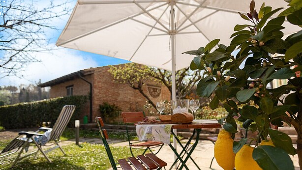 An outdoor seating area with a table set for dining, surrounded by greenery and a house in the background. - Regarda - Countryhouse Nocino 1 in the middle of Lake Garda vineyards (Lazise)