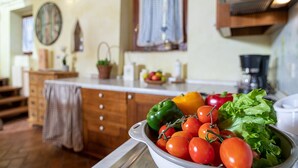 A kitchen with wooden cabinets, a fruit bowl, and a variety of fresh vegetables on the counter. - Regarda - Countryhouse Nocino 1 in the middle of Lake Garda vineyards (Lazise)