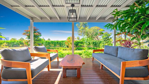 A covered outdoor seating area with wooden furniture and a view of a lush garden. - Nelson Bay CBD Oasis - 13 Government Rd (Nelson Bay)