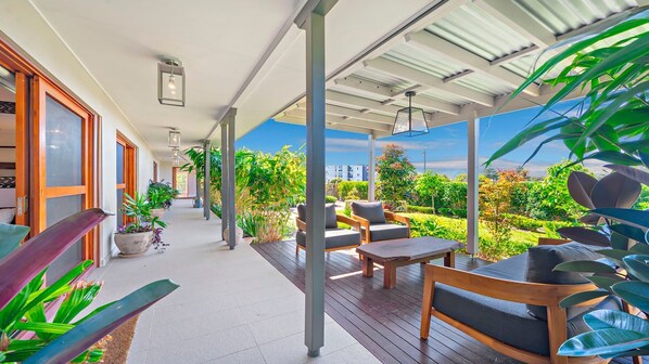 A covered outdoor area with wooden flooring, seating, and potted plants.