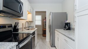 A modern kitchen with white cabinets, a stainless steel refrigerator, a microwave, and a coffee maker. - Historic charm blended with modern convenience! (Wrightsville Beach)