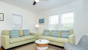 A living room with two light green sofas, a wicker coffee table, a grey armchair, and a ceiling fan. - Historic charm blended with modern convenience! (Wrightsville Beach)