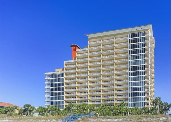 Un hotel de varios pisos con diseño moderno, que cuenta con balcones en cada planta y una chimenea roja destacada.