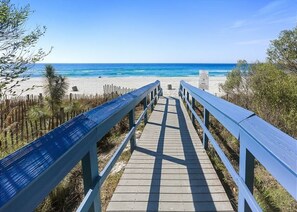 A wooden boardwalk leading to a beach with clear blue water and a sandy shore.