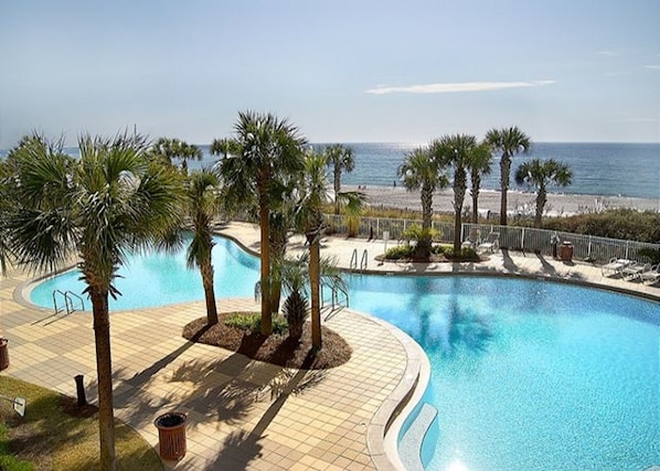 A pool area with palm trees and a view of the beach.