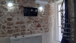 Une pièce avec un mur en pierre, un téléviseur à écran plat fixé au-dessus d’un meuble blanc et une fenêtre avec un rideau.
