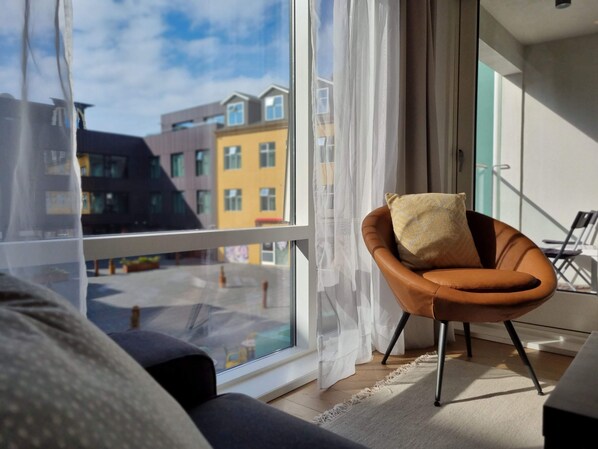 A modern living room with a large window, a brown leather chair, and a view of colorful buildings outside.
