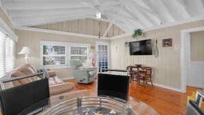 Un salón espacioso con techo alto, suelo de madera, un televisor montado en la pared y una zona de comedor con mesa y sillas.