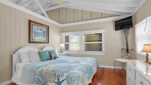 Un dormitorio con cama, un cuadro enmarco, una ventana con persianas, un televisor y una lámpara.