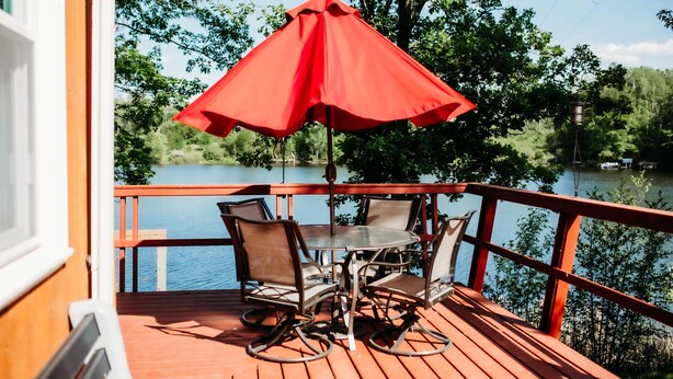Une terrasse en bois avec une table et des chaises, un parasol rouge et une vue sur un lac.