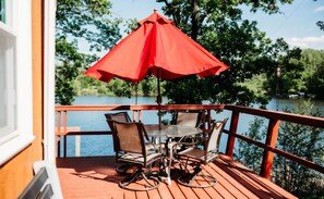A wooden deck with a table and chairs, a red umbrella, and a view of a lake. - Autumn Ridge North on Little Rabbit Lake (Ironton)
