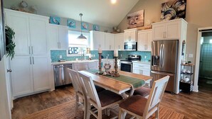 A modern kitchen with white cabinets, stainless steel appliances, and a dining area with a wooden table and chairs.