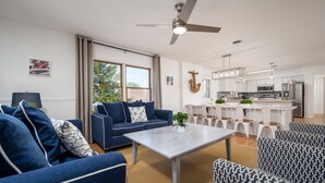 A modern living room with a blue sofa, a coffee table, and a dining area with white chairs. - Amazing location and layout for vacation fun! 206 Massachusetts (Lewes)