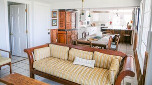 A cozy living room with a wooden sofa, a dining table, and a kitchen in the background.