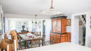 A dining area with a large white table, wooden chairs, and a traditional wooden cabinet.