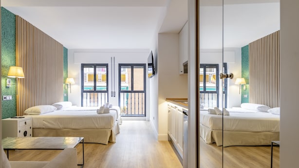 A hotel room with two beds, a desk, a chair, a TV, and a balcony with a view.
